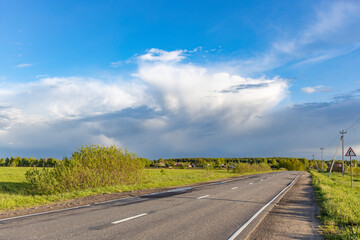 A road with a few trees in the background and a cloud in the sky