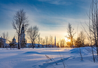 A snowy field with a church in the background and a sun setting