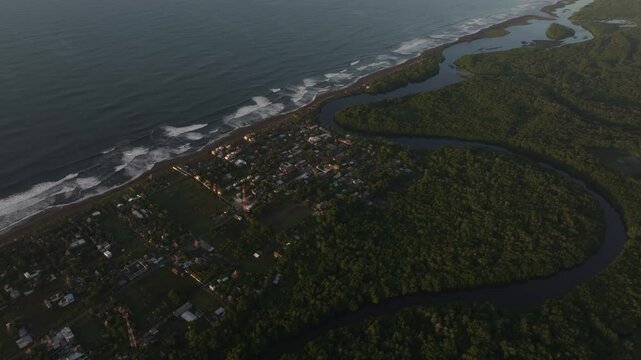 Aerial view of tranquil coastal village with lush forest and ripples in ocean, El Paredon, Guatemala.