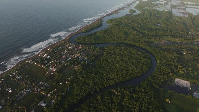 Aerial view of tranquil coastal town with tropical forest and shoreline, El Paredon, Guatemala.