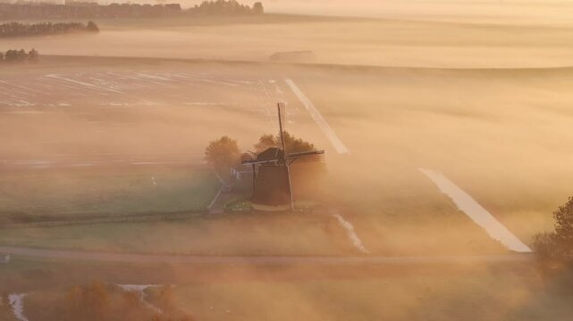 Aerial view of traditional windmill surrounded by foggy fields at sunrise, Workum, Friesland, Netherlands.