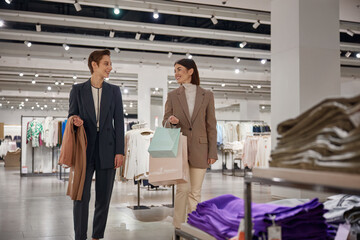 Happy young woman friends enjoying shopping together in big fashion shop mall