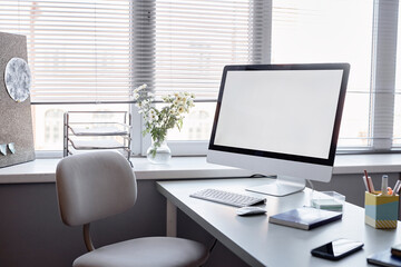 Still life shot of mockup screen of computer on desk in empty office or classroom next to window