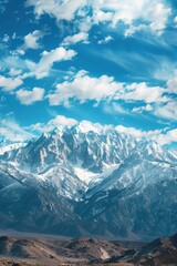 Obraz premium A mountain range covered in snow and a clear blue sky. The sky is dotted with clouds, giving the scene a serene and peaceful atmosphere
