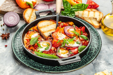 Delicious shakshuka breakfast in a frying pan with eggs, tomatoes, bell pepper, vegetables and herbs