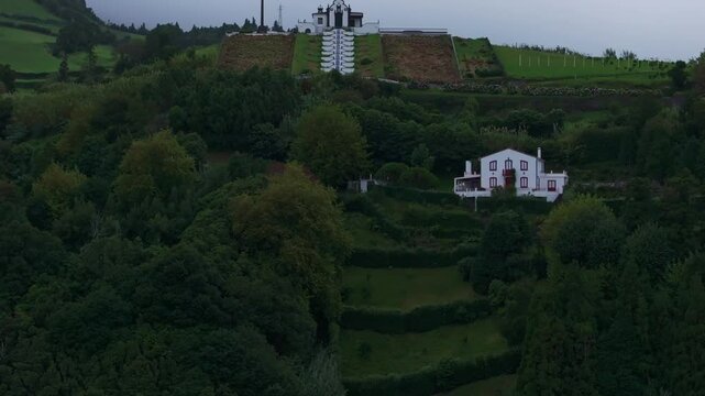 Aerial view of old church on hill with cross and white buildings, Ermida de Nossa Senhora da Paz, Azores, Portugal.