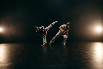 Couple of fighters training capoeira on black background