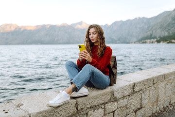 Beautiful woman with phone walking on city embankment. Tourist during holidays. Lifestyle, travel, nature, active life.