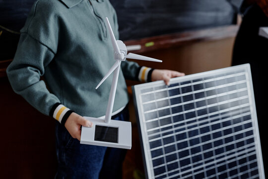 Close up on mini solar energy wind turbine and huge solar panel in hands of primary schoolboy presenting project about sustainable technology in class, copy space