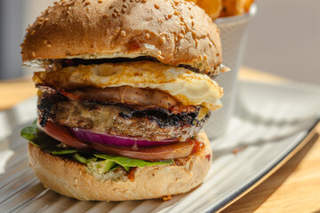 close up of a burger with egg, vegetable, beef and tomato, tomato sause and bun, hamburger on a white plate, fried chips in the background, fast food store, fast food culture