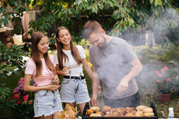 Family barbecue grill in the garden. Barbecue party. A family  is having fun and chatting on the grill. Bearded man with two girls are chatting on the grill. 