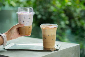hand of woman holding a take-out iced coffee with taro milk on cement table
