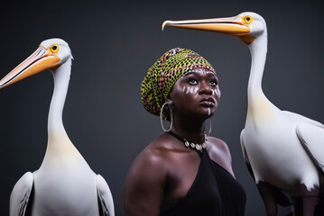 African woman with face painting and headdress with two birds in the background.