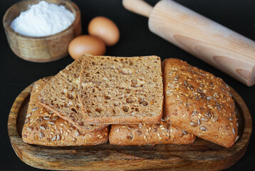 Small fresh breads with seeds and sesame on a wooden tray next to eggs, a wooden bowl with flour and a rolling pin