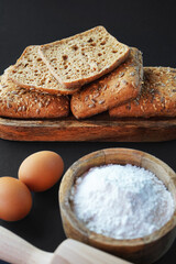 Small fresh breads with seeds and sesame on a wooden tray next to eggs, a wooden bowl with flour and a rolling pin