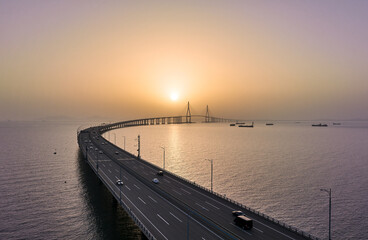 Songdo-dong, Yeonsu-gu, Incheon, South Korea - April 16, 2023: Aerial and sunset view of cars driving on curved road of Incheon Bridge on the sea against horizon
