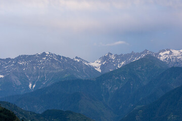Sunlit snow-capped mountain peaks towering over a blanket of forested hills