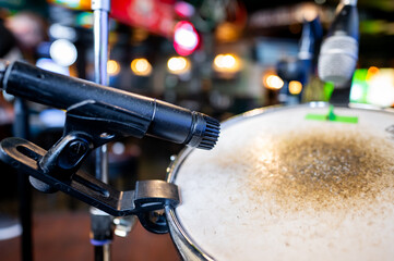 Close-up of a microphone attached to a drum set with blurred lights in the background, capturing a...