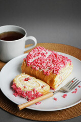 Sponge roll with cream and pink sprinkles on a white plate next to a fork and cup on a gray background