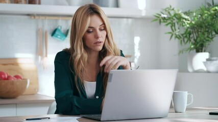 Video of stressed business woman working from home on laptop looking worried, tired and overwhelmed int he kitchen at home. - Powered by Adobe