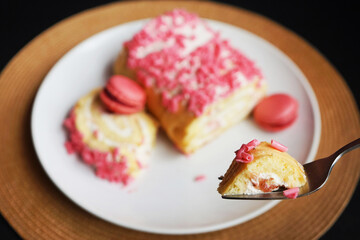 A piece of sponge cake on a fork against a background of roll with pink sprinkles and raspberry macaroons on a white plate