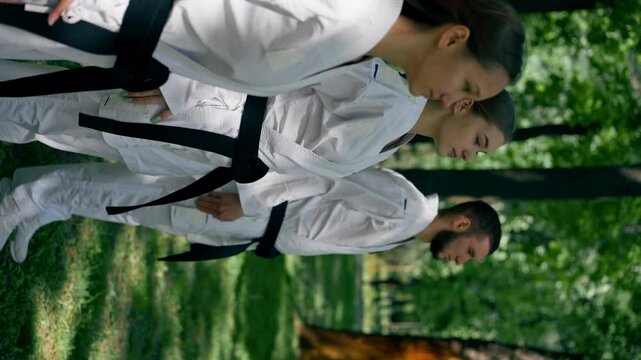 vertical video outdoors in the park in sunny weather young karatekas are warming up using the karate technique martial arts black belt healthy lifestyle combat training