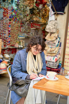 Woman writing in notebook at a quaint outdoor caf� table surrounded by colorful accessories.