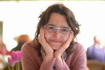 Smiling woman with round glasses resting her chin on her hands next to a pink tulip
