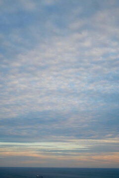 Sunset sky with altocumulus clouds over a calm ocean with a visible ship on the horizon.