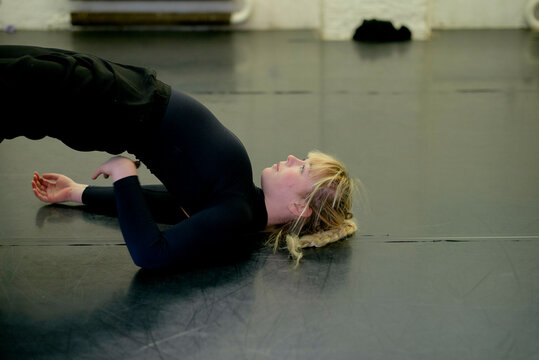 Woman practicing a bridge pose on a black mat in a dance studio.
