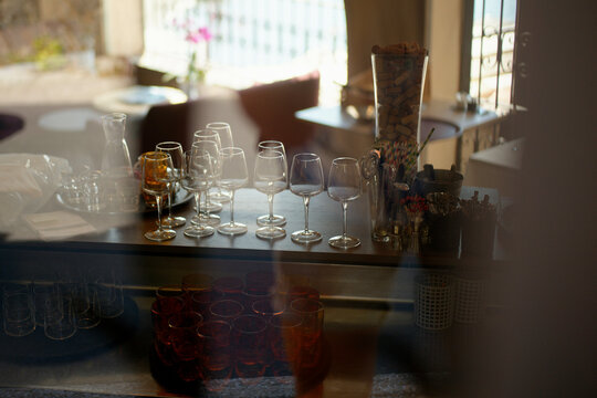 Evening sunlight filters through a window, casting a warm glow over an assortment of empty wine glasses arranged neatly on a bar counter.