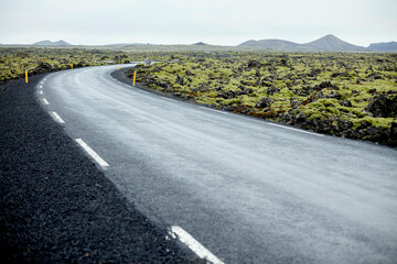 A curving asphalt road surrounded by a rugged lava rock landscape under a cloudy sky. Iceland