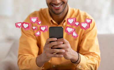 Cropped of man smiles as he uses his phone. There are several small pink hearts with white inside them in speech bubbles, floating around his hands and head