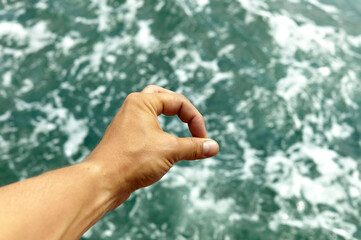 Hand forming an OK gesture against a blurred ocean background