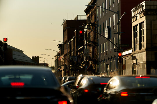 Evening traffic on a city street with red stoplights and the sun setting behind buildings casting a warm glow.