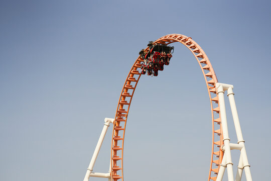 Roller coaster at the peak of a loop against a clear blue sky.