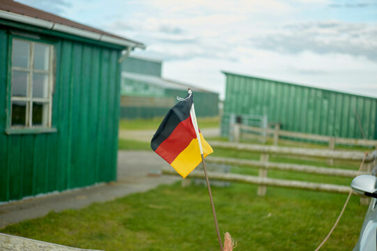 German flag fluttering in front of green wooden buildings in a rural setting