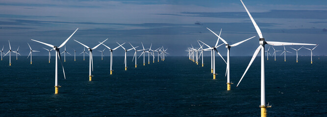 Offshore wind farm with multiple turbines standing in the sea under a bright blue sky.