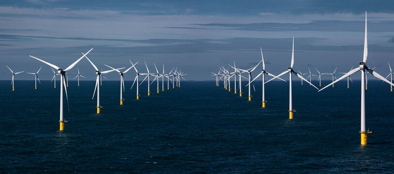 Offshore wind farm with rows of wind turbines in the ocean under a cloudy sky.