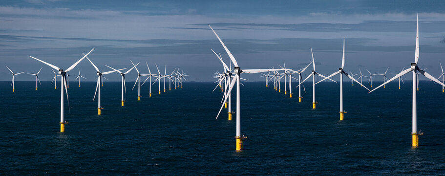 Offshore wind farm with several wind turbines standing in the ocean under a blue sky.