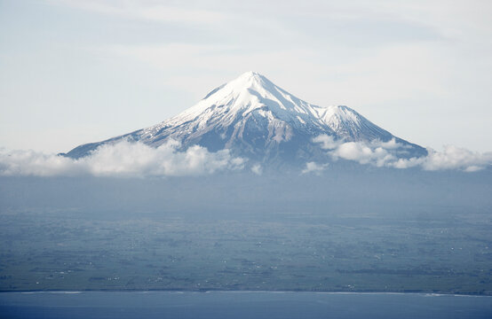 Snow-capped mountain peak rising above the clouds, with a clear view of the summit and a hint of the surrounding landscape below, Mt. Taranaki, New Zealand