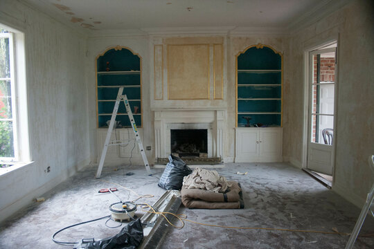 An interior view of a room undergoing renovation with tools and a ladder present, exposed wall sockets, and a fireplace.