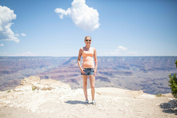 Smiling woman standing at the edge of the Grand Canyon on a sunny day with a clear blue sky and fluffy clouds overhead.