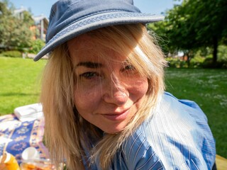 Close-up of a smiling woman wearing a blue hat and striped shirt at a sunny park picnic.
