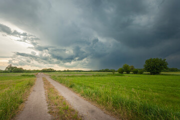 Rural road through green fields and storm clouds in the sky