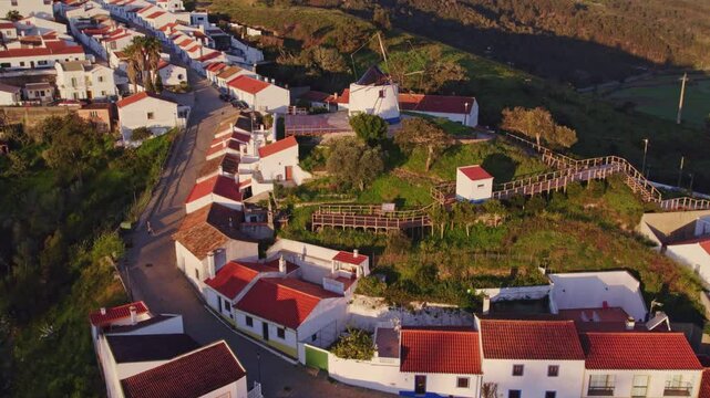 Aerial view of charming European village with windmill, red roofs, and greenery, Odeceixe, Portugal.