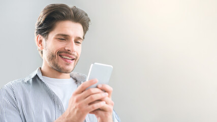 Cheerful millennial man texting with friend on cellphone, empty space