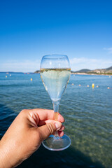 Obraz premium Summer time in Provence, hand with glass of cold champagne cremant sparkling wine on famous Pampelonne sandy beach near Saint-Tropez in sunny day, Var department, France, beach club party