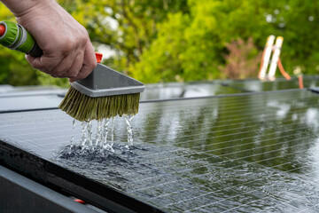 Close-up of a hand using a brush to clean a solar panel with water splashing.