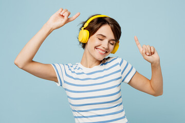 Young smiling happy woman wear striped t-shirt casual clothes listen to music in headphones raise...